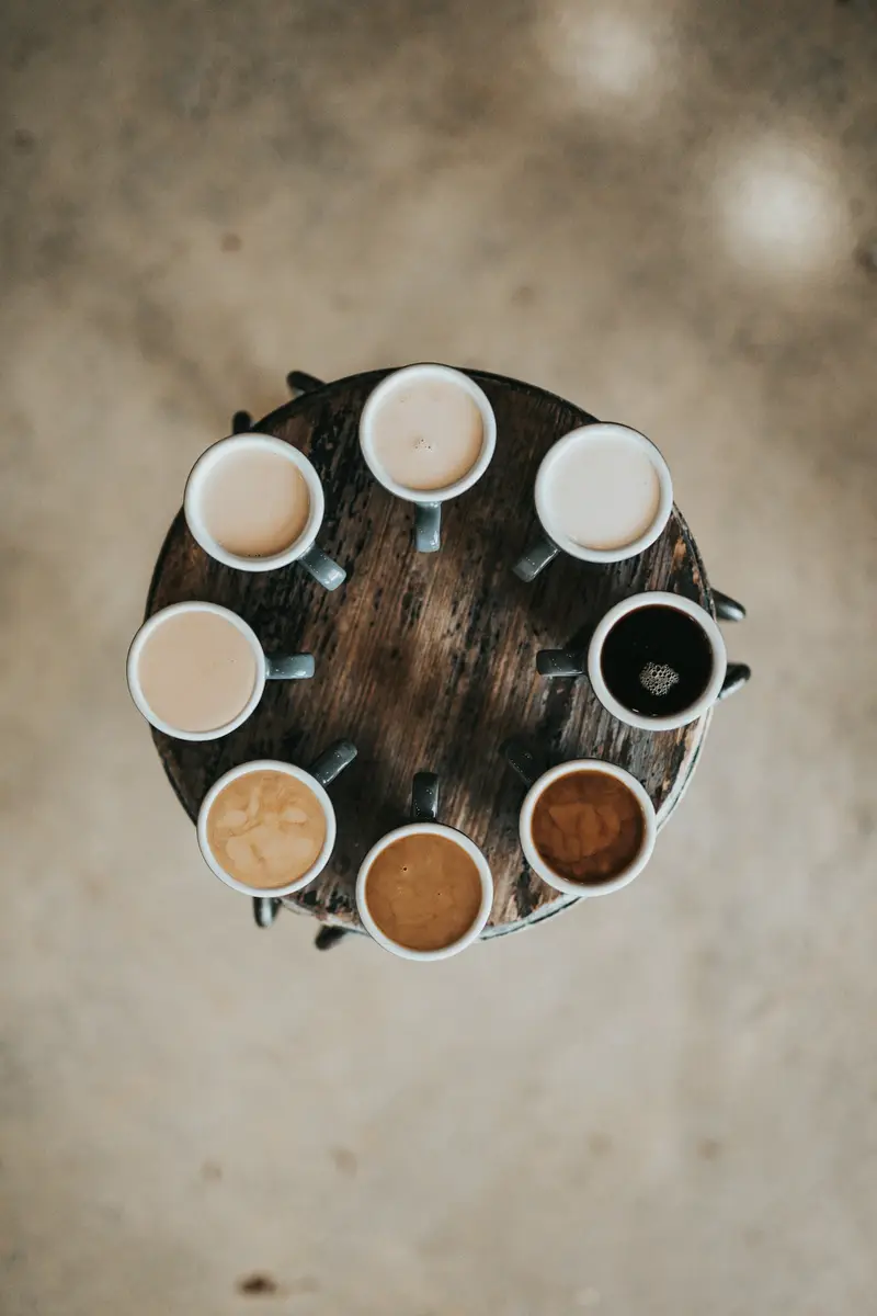 Nine cups of coffee arranged in a circle on a wooden table, seen from above