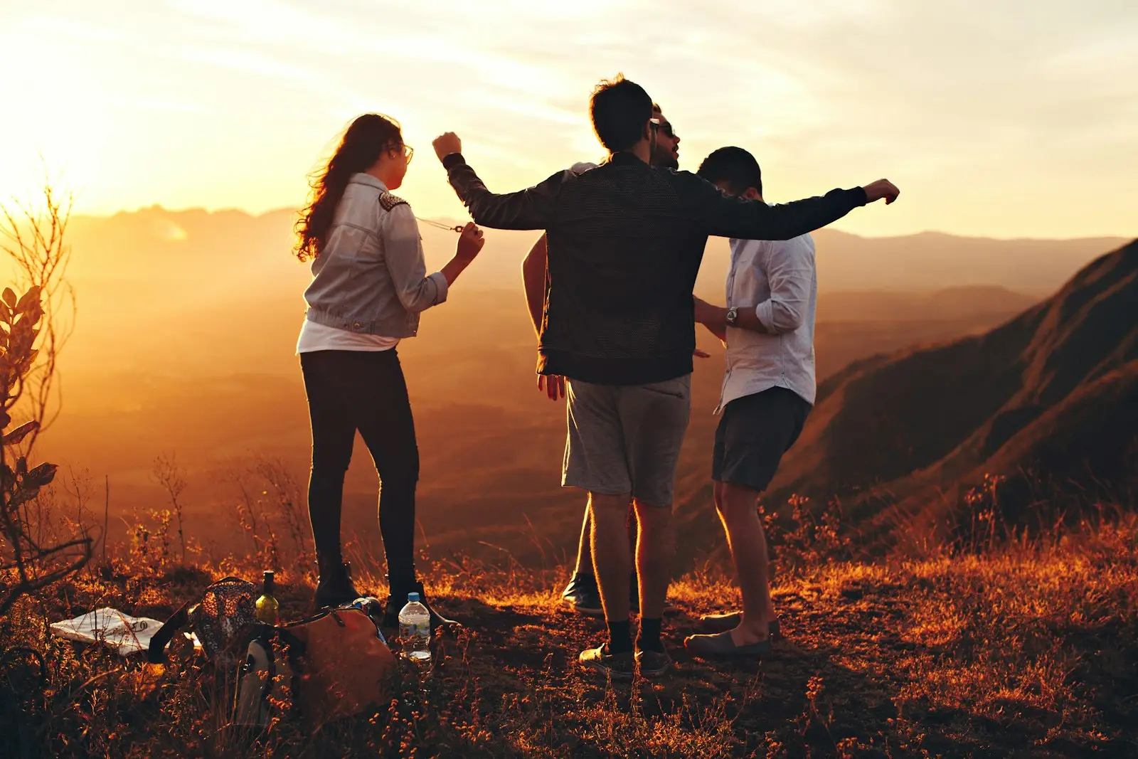 Three people in silhouette on a hilltop at sunset, arms raised, faces turned away