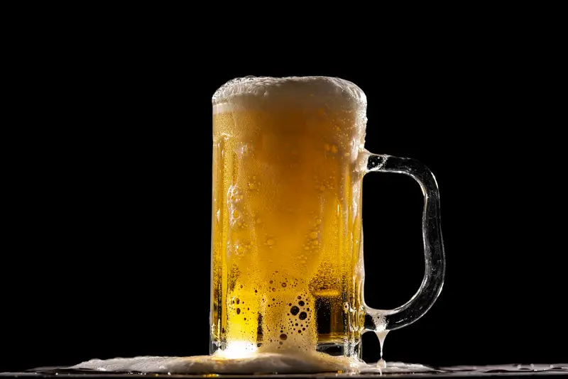 A full glass of beer with a thick head, against a dark background