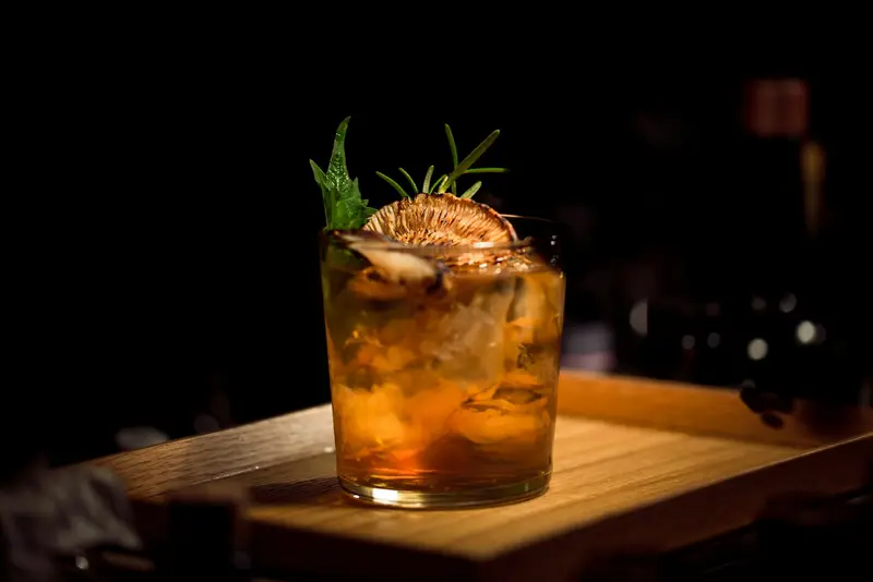 A short glass of spirits over ice on a dark bar top